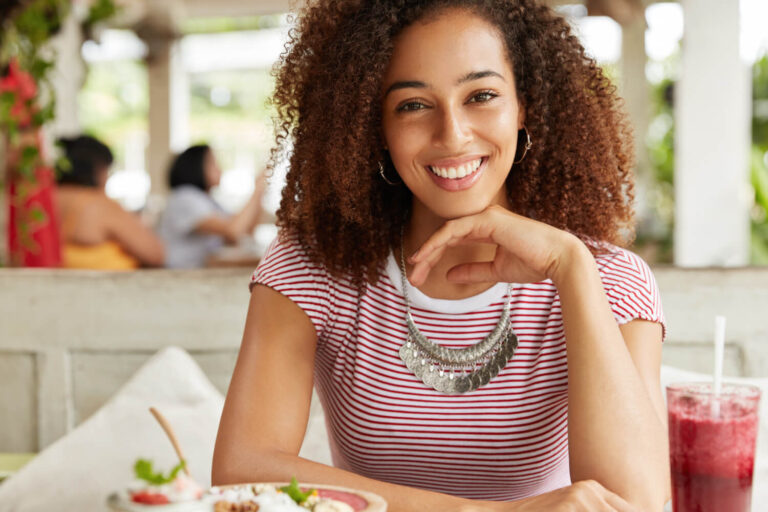 Mulher sorridente com dentes brancos e alinhados em restaurante, representando restauração dos dentes da frente na Aoun Implantes em Guarulhos.