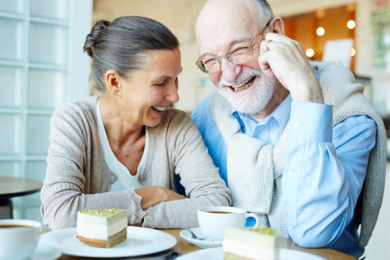 Casal idoso sorrindo ao comer sobremesa, celebrando o sucesso do implante dentário na Aoun Clínica Odontológica em Guarulhos.
