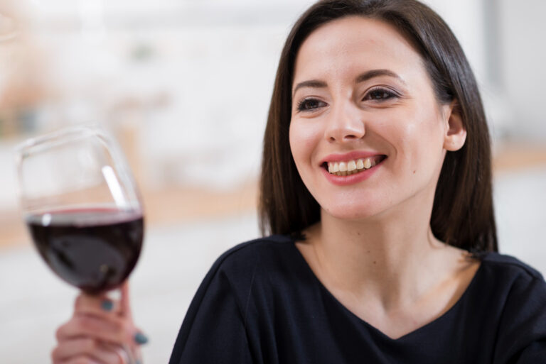 Mulher jovem sorrindo ao segurar taça de vinho tinto, ilustrando a resistência das lentes de contato dental na Aoun Clínica em Guarulhos.