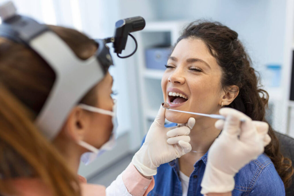 Dentista com espelho clínico examina dentes de paciente na Aoun Odontologia em Guarulhos para clarear restauração de resina antiga.