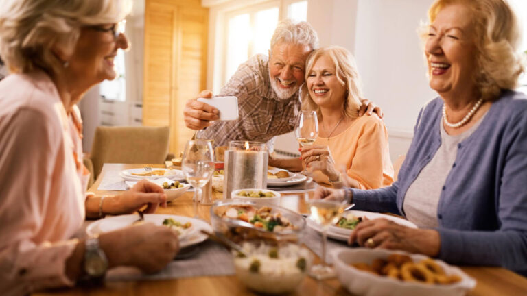Idosos felizes jantando e rindo muito ao redor da mesa, livres do medo de a prótese dentária móvel soltar ao falar ou comer em Guarulhos.