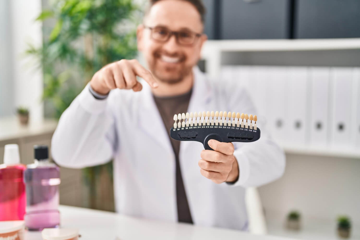 Dentista em jaleco aponta para escala de tons para escolha da cor da coroa do implante dentário na Aoun Odontologia em Guarulhos.